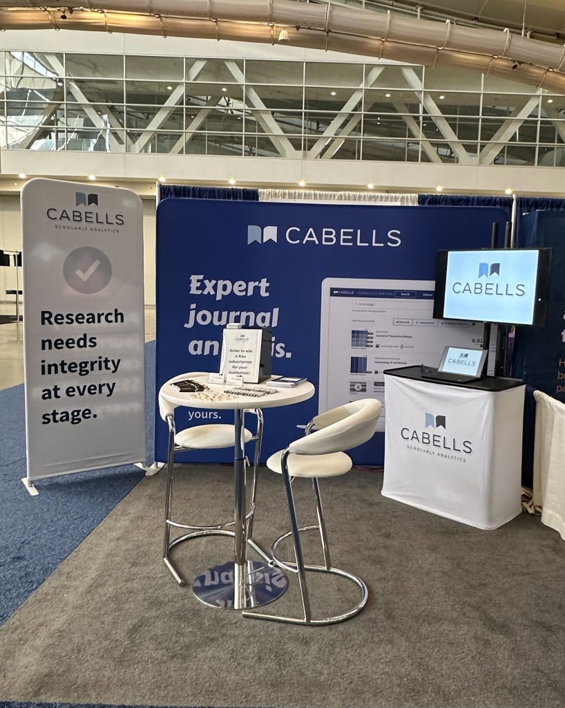 A Cabells booth at the Medical Library Association conference featuring banners that read 'Research needs integrity at every stage' and 'Expert journal analysis.' The booth includes a circular table with chairs and a screen displaying analytics.